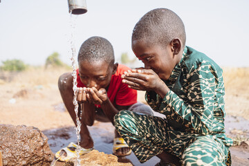 Two thirsty siblings drinking fresh water from a remote tap in the steppe of rural sub-Saharan...