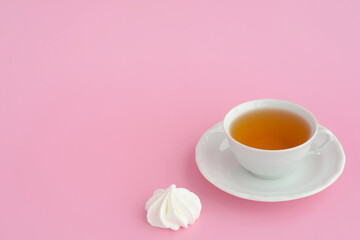 A cup of tea and marshmallows on a pink table background, copy space. Black tea and sweets, tea time