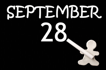 A small white plasticine man writing the date 28 September on a black board. Business concept. Education concept.