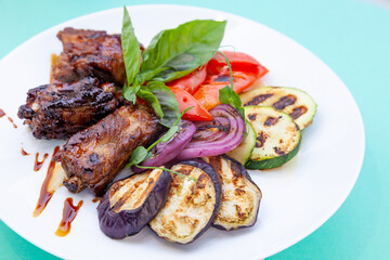 Grilled meat and vegetables. Zucchini, peppers, red onions and basil. Fried pork medallions. Food on a white plate in a restaurant