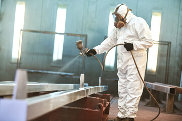 industrial painter in chamber spraying paint on metal detail - 496109714