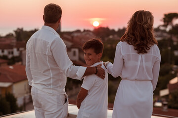 Happy family enjoys and spends time together on the roof of the house while watching the sunset on the open sea together
