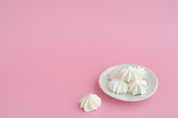 Vanilla homemade meringues a plate on pink table background, copy space. White marshmallows a plate