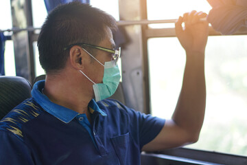 Asian male passenger wears hygienic face mask and sun glasses, sits on bus. Concept : 
Protecting...