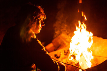 young man sitting near fire in camping in summer night
