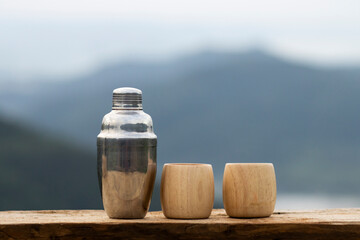 selective focus stainless steel thermal water bottle and bamboo coffee mug placed on a wooden balcony natural mountain background Leave space for text