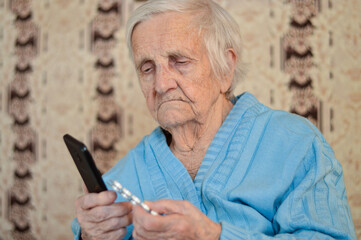 Close up of a 90-year-old sick pensioner who holds a package of pills and a phone in her hands.