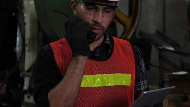 Middle eastern foreman or worker using digital tablet to examine production line, found problem, being worried, using walkie-talkie radio to communicate or signal the danger to others. Factory concept