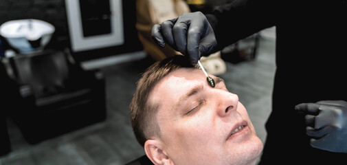 Visit to barbershop.Wax depilation,hair removal between the eyebrows.Stylish man makes fashionable...