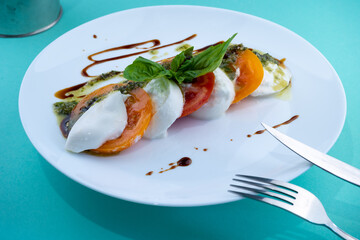 Caprese salad with tomatoes, mozzarella and basil. Red and orange tomatoes with white cheese and sauce. Portion of food on a plate in a restaurant. View from above. Delicious healthy food.