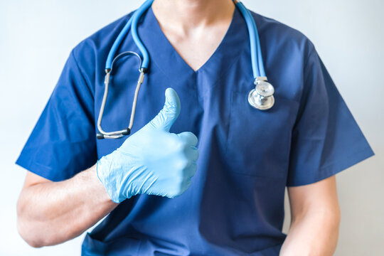 Cropped image of handsome male surgeon doctor with stethoscope in blue uniform with statoscope holding thumb up in clinic on blue background. banner with copy space
