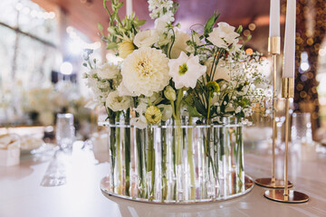 Wedding. Banquet. The festive table is decorated with compositions of white flowers and greenery on decorative stands. There are glasses, candles and cutlery on the table.