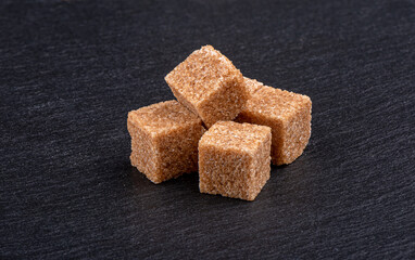 A few pieces of cane sugar on a dark stone surface.