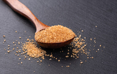 Cane sugar on a wooden spoon over a dark surface with space for text.