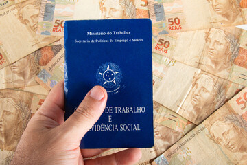 Hand holding Brazilian document work and social security (Carteira de Trabalho e Previdencia Social) with fifty reais banknotes. brazilian money
