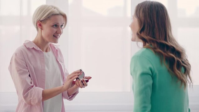 Blond lesbian woman making proposal to her girlfriend, showing engagement ring