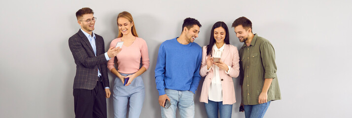 Group of young millennial and generation Z people using mobile phones. Happy male and female office colleagues leaning on wall, connecting to free wifi, reading news, looking at memes, text messaging
