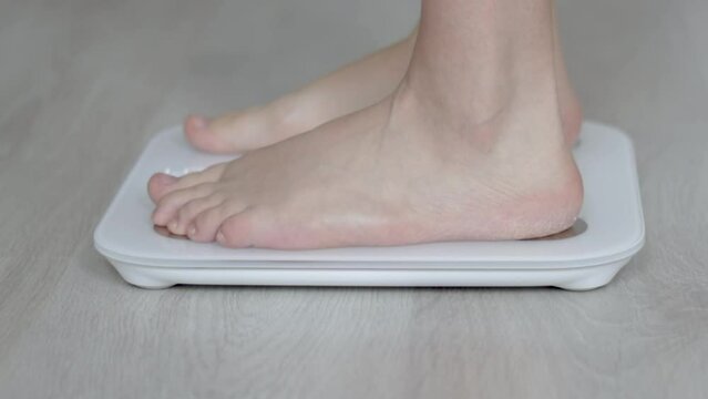 young woman or man is sitting or steping on modern scale for weight measurements. body fat scale accurate. body composition monitor, white color on grey floor. weight control. diet and fitness concept