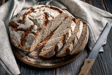 Homemade rye bread. Sliced rye bread in a round shape on a wooden background in a rustic style with towel and bread knife