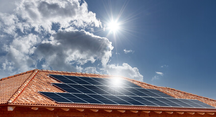 Roof with solar panels on blue sky with reflecting sun rays © framarzo