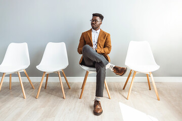 Male entrepreneur waiting for job interview in a hallway. He's the last one left to be interviewed. Full length studio shot of a handsome young businessman sitting against a gray background