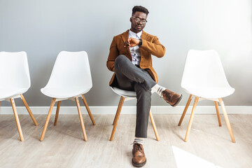 Full length shot of a handsome young businessman sitting and looking down at his watch against a gray studio background. I'm getting bored waiting for them - obrazy, fototapety, plakaty