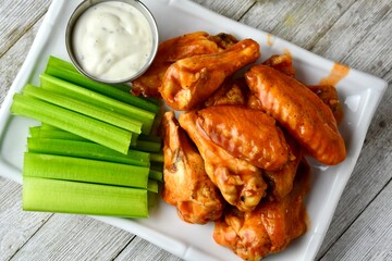 top down view of a plate of buffalo wings with celery sticks and ranch dressing on a wooden table