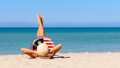A tanned girl on the beach in a straw hat in the colors of the flag of the Malaysia. The concept of a perfect vacation in a resort in the Malaysia. Focus on the hat.