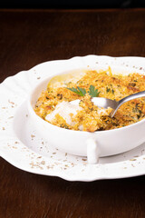 fish casserole focus on spoon showing cheese and crispy breaded food and blurred plate