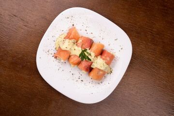 plate of fresh smoked salmon rolled up stuffed with cream cheese and parsley on wooden table.centered top view