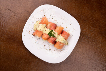 plate of fresh smoked salmon rolled up stuffed with cream cheese and parsley on wooden table.centered top view