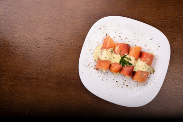 plate of fresh smoked salmon rolled up stuffed with cream cheese and parsley on wooden table.top view