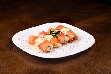 plate of fresh smoked salmon rolled up stuffed with cream cheese and parsley on wooden table