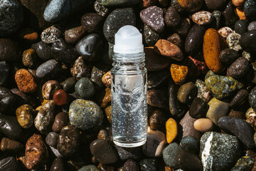 Flat lay composition of a roll on transparent deodorant bottle on wet beach stones . Fresh ocean...