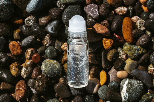 Flat lay composition of a roll on transparent deodorant bottle on wet beach stones . Fresh ocean scented product mock up. 