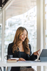 Young brunette Asian businesswoman using tablet feeling happy at desk in modern desk.