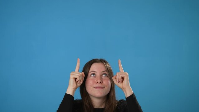 Happy promoter secret young brunette woman 20s wears black shirt pointing fingers up on workspace copy space mockup promo commercial area isolated on pastel plain light blue background studio portrait