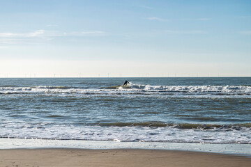 Silhouette of a surfer on a surfboard among sea waves, selective focus. Seascape with the North Sea in the Netherlands.