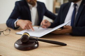 Close up of judge gavel against background of professional lawyers discussing legal case. Judge's dark dark-brown hammer standing on sound block on table. Blurred background.