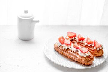 Eclairs with cream and strawberries on a white plate. 