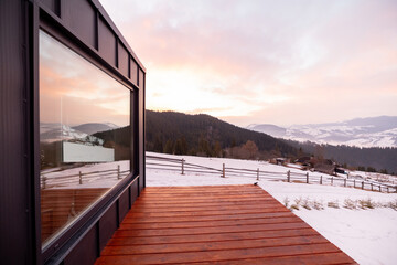 Tiny house with terrace and big window in the mountains during winter on sunrise. Concept of small...