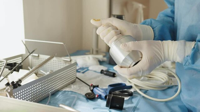 Close up of female hands in sterile gloves holding trocar for laparoscopy procedure. Laparoscopic scissors and graspers on blue desk. Multifunction Laparoscopic Instruments