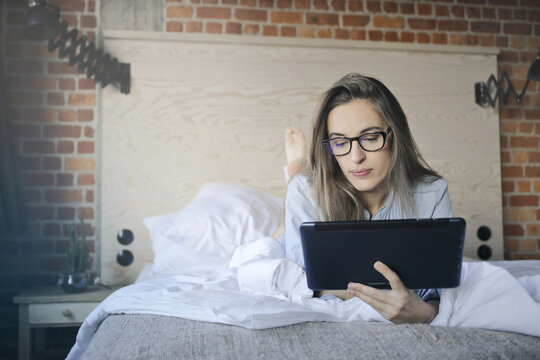 young woman lying on a bed uses a tablet