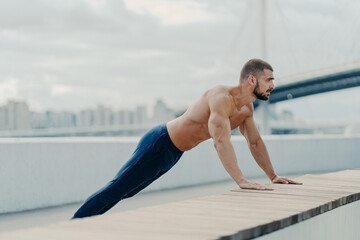 Athlete guy stands in plank pose does push up exercise outdoor breathes fresh air has strong body...
