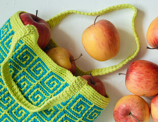 Modern blue yellow crochet bag for shopping with fresh red apples on a white background. Colored...