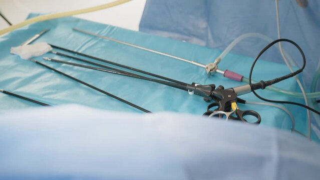 Laparoscopic scissors and graspers on blue desk. Multifunction Laparoscopic Instruments. Close up of female hands in sterile gloves holding trocar for laparoscopy procedure