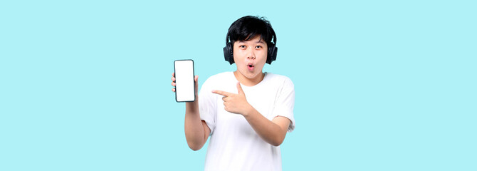 Shock and surprise face of tomboy Asian presenting smart phone and earphones on blue background in...
