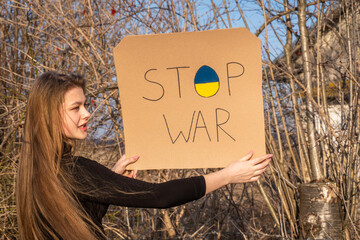 Upset adult woman holds banner protesting the war between Russia and Ukraine. Female asks to stop...