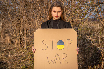 Upset woman holds banner protesting the war between Russia and Ukraine. Female asks to stop the...