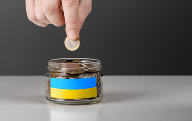 donation for ukrainian refugees. donation jar with Ukrainian flag. Hand putting Coins in glass jar...